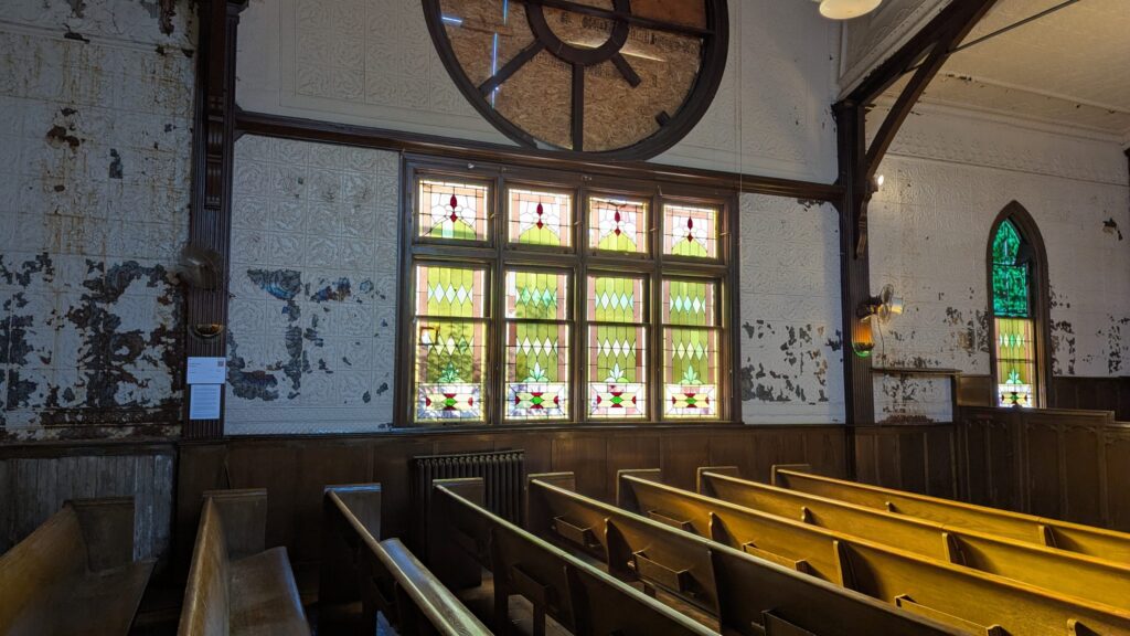 The interior of the west wall of the old church at Hermitage and Diamond, the late afternoon sun shining through the stained glass window.